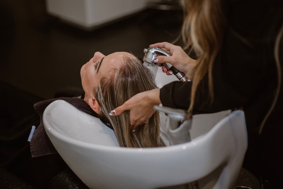 A stylist washing a client’s hair at a salon basin